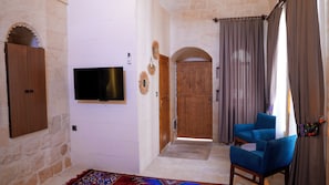 Una habitación con un televisor de pantalla plana montado en la pared, una puerta de madera, un sillón azul y una alfombra estampada.