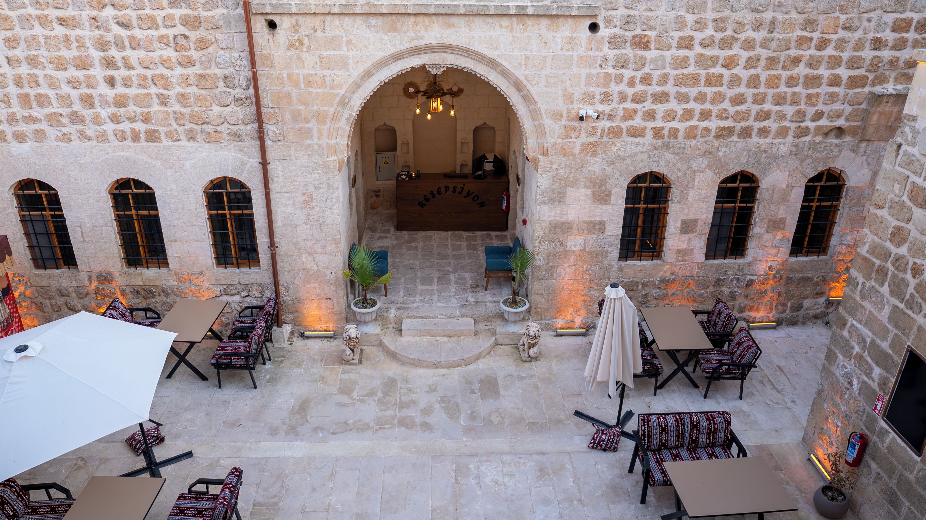 A courtyard with stone walls, a central archway, and outdoor seating with tables and chairs.