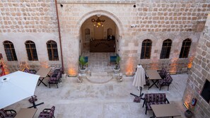 A courtyard with stone walls, a central archway, and outdoor seating with tables and chairs. - Sargon Hotel & Cafe (Midyat)