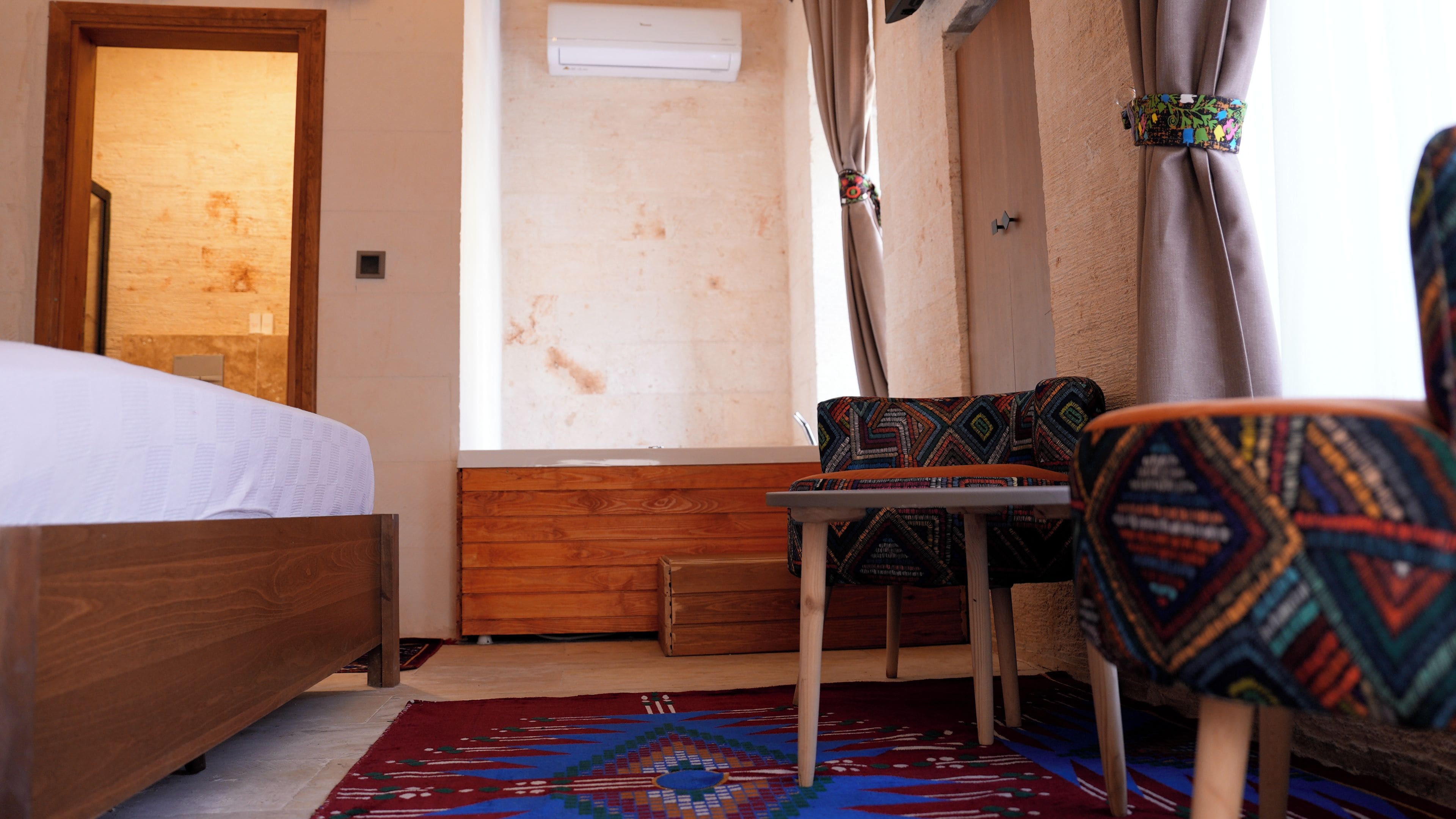 A room with a wooden bed, a small table, a patterned chair, and a window with curtains.