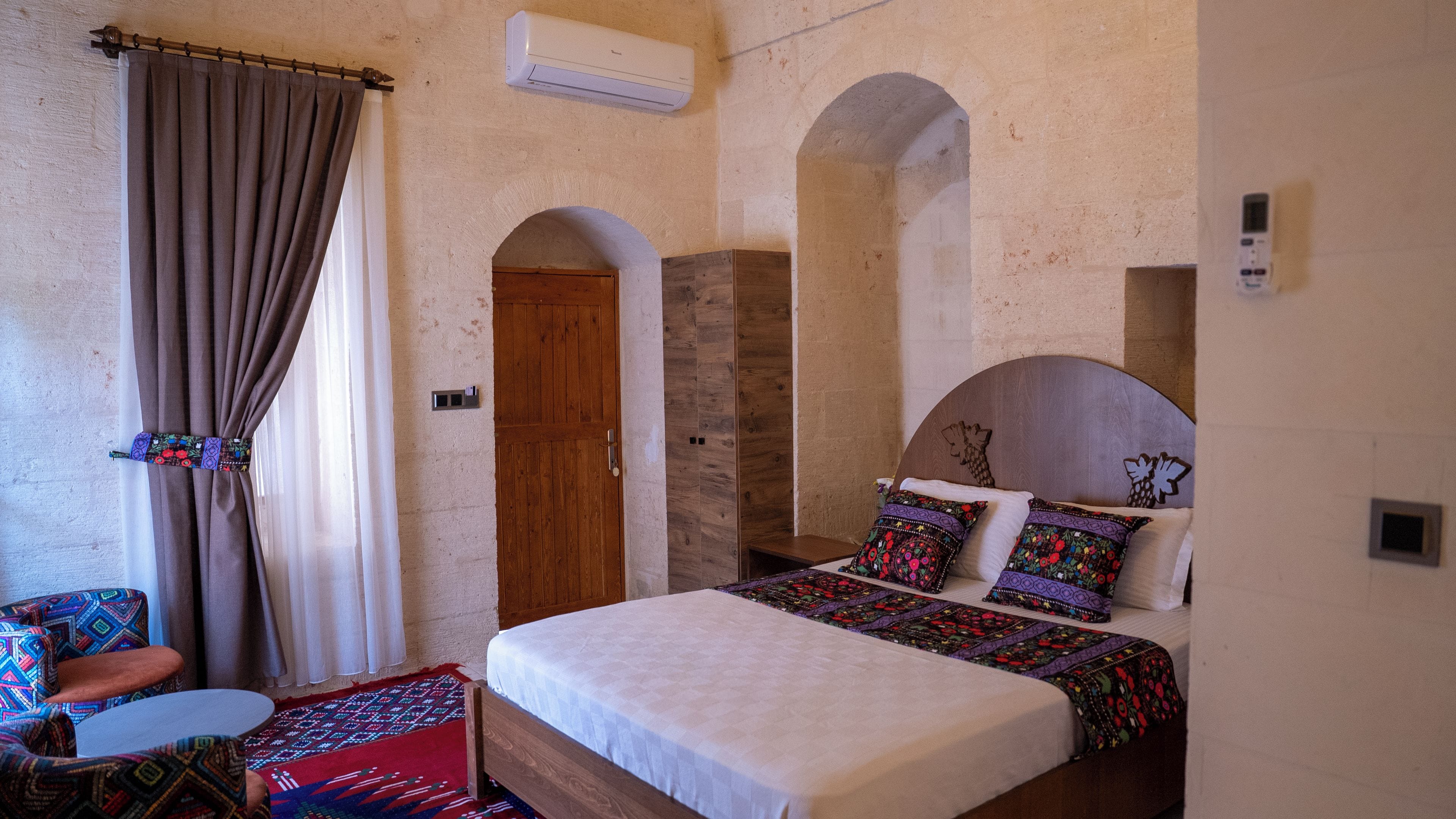 Quarto com cama, porta de madeira, aparelho de ar condicionado e janela com cortinas.