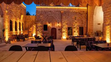 Un área de comedor al aire libre con paredes de piedra, mesas y sillas de madera.
