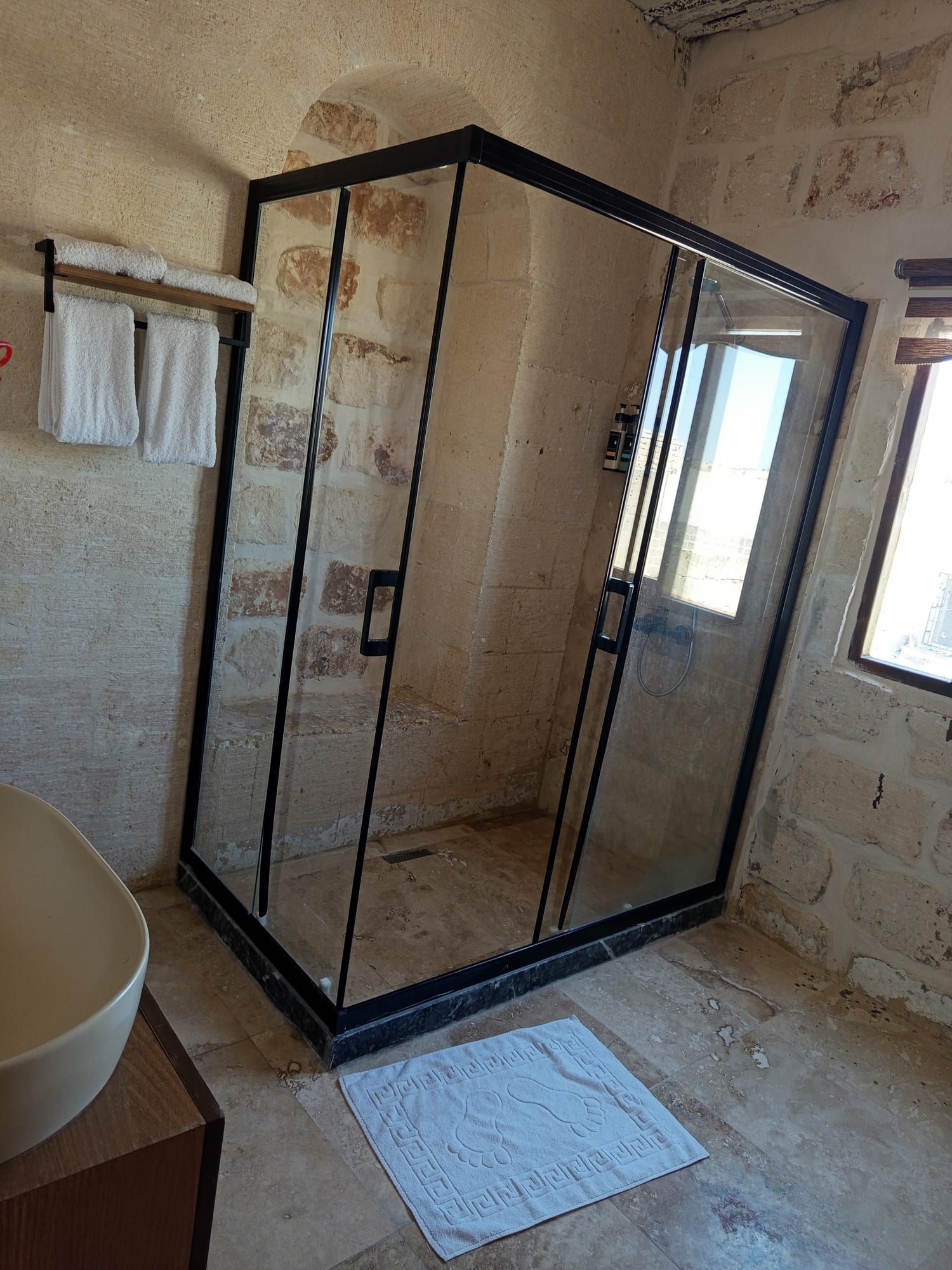 A glass-enclosed shower area with a tiled floor, a towel rack, and a visible window.