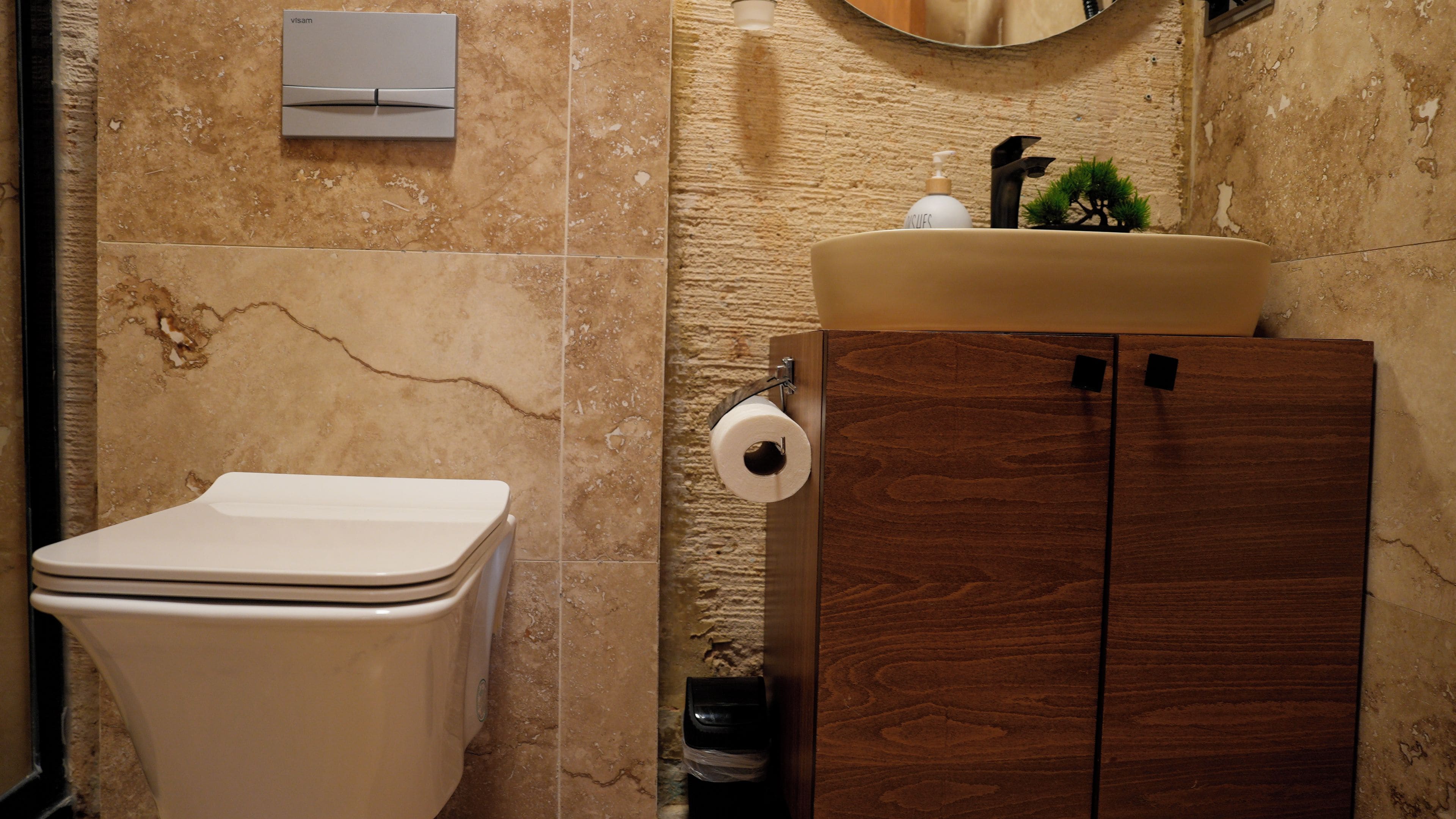 Un baño con inodoro, un armario de madera, un lavabo con dispensador de jabón y un soporte para papel higiénico.