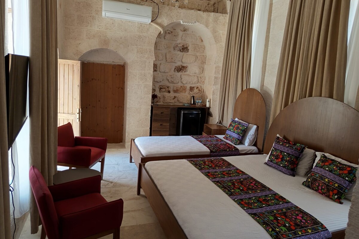 Un dormitorio con dos camas, un escritorio, una silla y una pared de piedra.