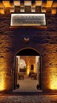 Entrada do Hotel & Cafe Sargon, com um arco de pedra e uma placa acima.