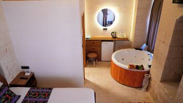 A room with a bed, a small stool, a round wooden bathtub, a mirror, and a wooden cabinet.