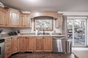 A kitchen with wooden cabinets, a stainless steel dishwasher, and a window overlooking a rocky outdoor area. - Walk to Ski Lifts | 2 Living Areas | Sleeps 8 (Brian Head)