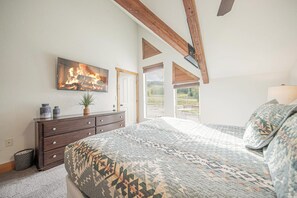 A bedroom with a large bed, a dresser, a painting of a fire, and a view of the outdoors. - Walk to Ski Lifts | 2 Living Areas | Sleeps 8 (Brian Head)