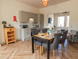 A modern kitchen with grey cabinets, a wooden herringbone floor, and a dining area with a table set for two. - Sandy Toes (Annan)