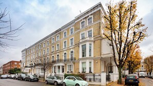 Un edificio residenziale a più piani con uno stile architettonico classico, caratterizzato da una facciata simmetrica, numerose finestre e un ingresso principale con viale recintato.