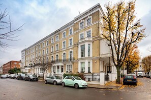 En flervåningsbostadsbyggnad med en klassisk arkitektur, kännetecknad av en symmetrisk fasad, många fönster och en framträdande entré med en uppfart som har grindar.