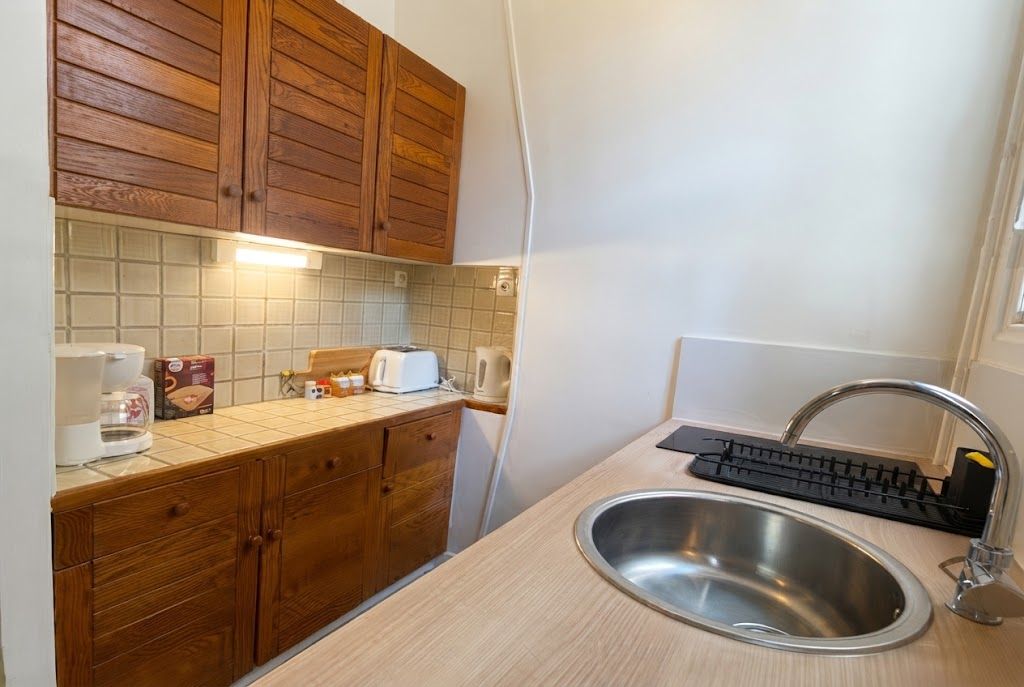 Een kleine keuken met houten kastjes, een roestvrijstalen spoelbak en een aanrecht met een broodrooster en koffiezetapparaat.