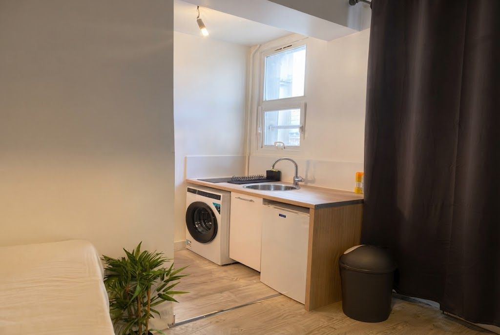 Een compacte kitchenette met een wasmachine, een spoelbak en een kleine prullenbak.