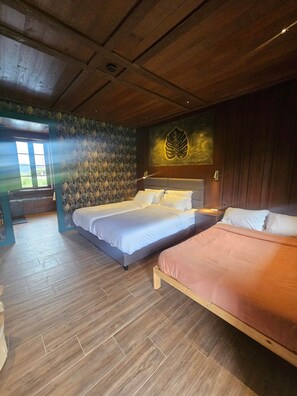 Habitación de hotel con dos camas, techo de madera, pared con diseño de hojas y una ventana.