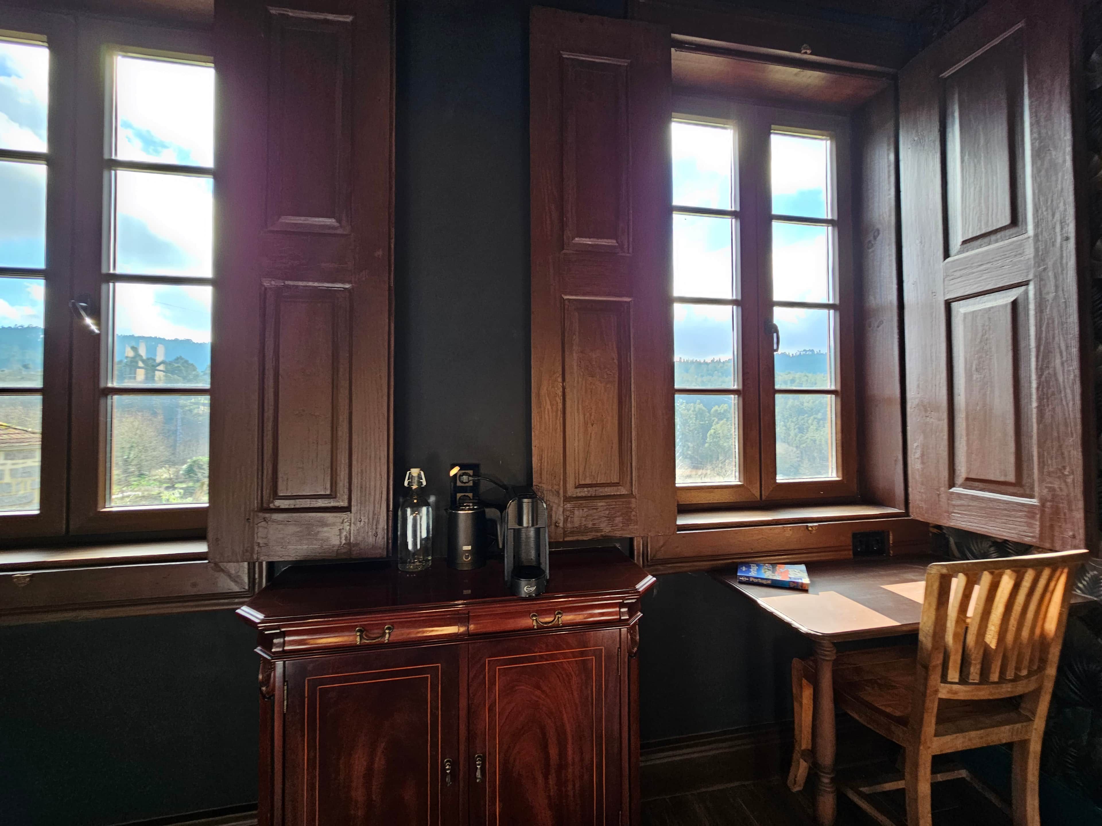 A room with a bay window, a wooden desk, a chair, and a cabinet with a view of the outdoors.