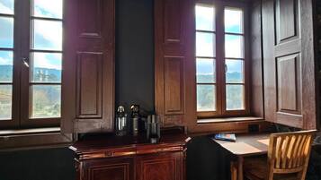 A room with a bay window, a wooden desk, a chair, and a cabinet with a view of the outdoors.