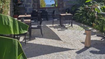 An outdoor patio area with stone flooring, tables, chairs, and a large plant.
