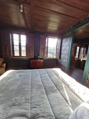 Ein Zimmer mit einem großen Bett, Holzboden und Fenstern mit Vorhängen.