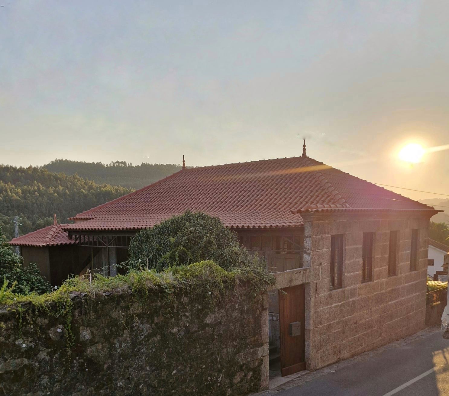 A building with a red-tiled roof, a stone wall in the foreground, and a clear sky.