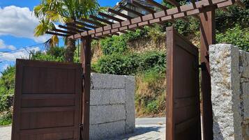 Une entrée fermée par un portail, agrémentée d’une pergola en bois, de murs en pierre et d’un chemin pavé.