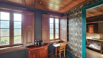 A room with a wooden ceiling, a dining table with chairs, a kitchen area with cabinets, and a view through the windows.