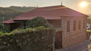 A two-story building with a red-tiled roof, a stone wall in front, and a clear view of the surrounding landscape. - Deluxe Three-Bedroom Vila 3 Bathrooms, incl Breakfast (Jugueiros)