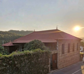 Un bâtiment à deux étages, avec un toit recouvert de tuiles rouges, un mur de pierre à l’avant et une vue dégagée sur le paysage environnant.