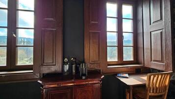 Una habitación con un escritorio de madera, una silla y un ventanal con contraventanas abiertas.