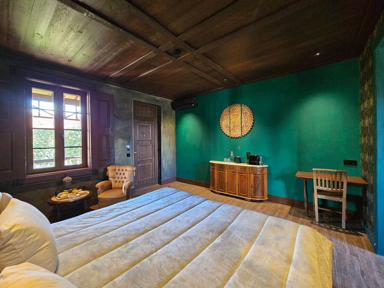 Un dormitorio con una cama grande, una silla de madera, un armario de madera y una pared verde.