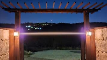 Un arco de piedra con una pérgola de madera arriba, que conduce a un área pavimentada.