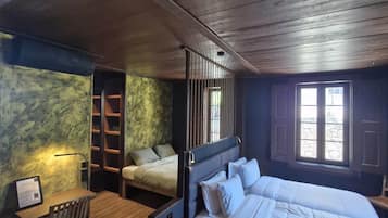 A bedroom with a large bed, a desk, and a chair. There is a window with a view of the outside.