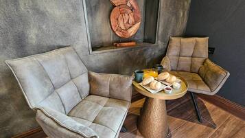 Ein Zimmer mit zwei Polstersesseln, einem runden Holztisch mit Frühstücksgebäck und einer an der Wand befestigten Holzskulptur.