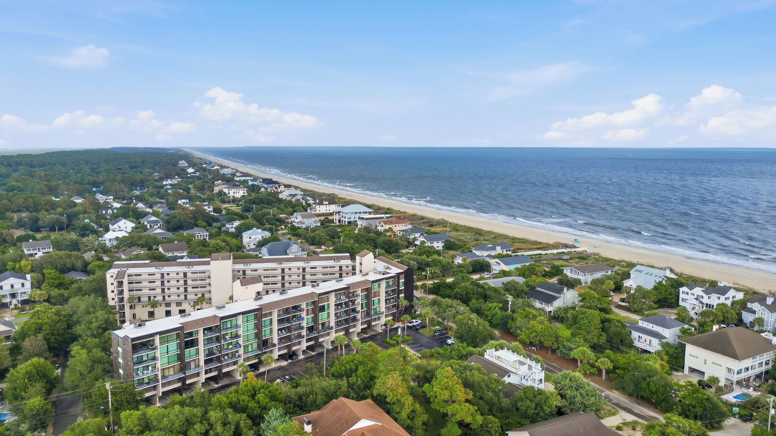 A coastal residential area with a beachfront, a multi-story building with balconies, and a clear view of the ocean.
