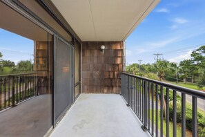 A balcony with a metal railing, a glass door, and a view of greenery and a road. - Litchfield By The Ocean, Two bedroom condo across from Litchfield Beach (Pawleys Island)