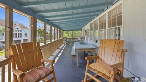 Eine überdachte Veranda mit Holzstühlen und einem Tisch, mit Blick auf eine Wohngegend.