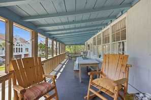 Eine überdachte Veranda mit Holzstühlen und einem Tisch, mit Blick auf eine Wohngegend.