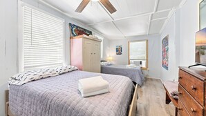 Ein Schlafzimmer mit zwei Betten, einem Deckenventilator, einem Kleiderschrank und Kunstwerken an den Wänden.