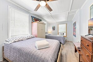 Ein Schlafzimmer mit zwei Betten, einem Deckenventilator, einem Kleiderschrank und Kunstwerken an den Wänden.