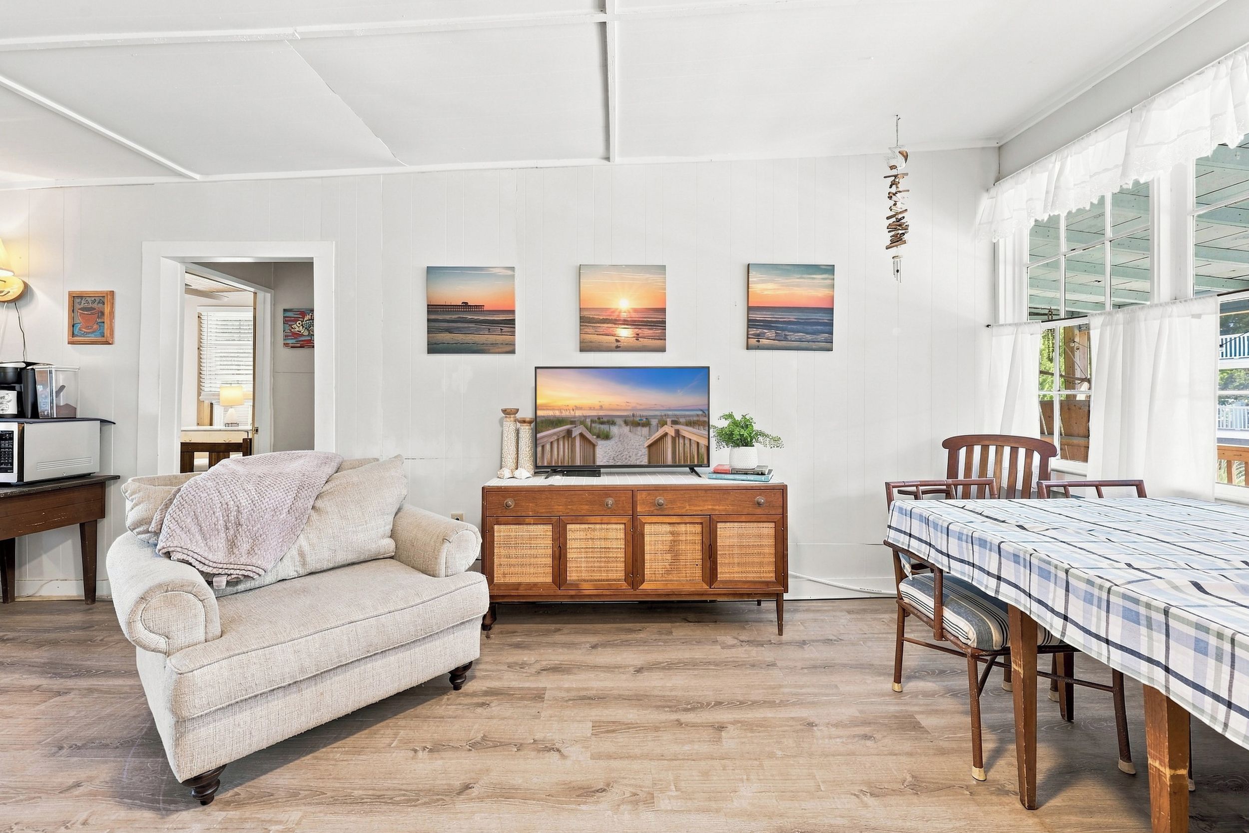 A cozy living room with a sofa, wooden dining table, and artwork on the walls.