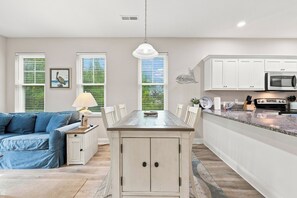 A modern kitchen with white cabinetry, a central island, and a dining area with a blue sofa. - Murrells inlet Peeps (Murrells Inlet)