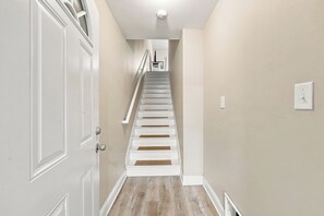 A staircase with white steps and a handrail, leading to a landing with a light switch and a small shelf. - Murrells inlet Peeps (Murrells Inlet)