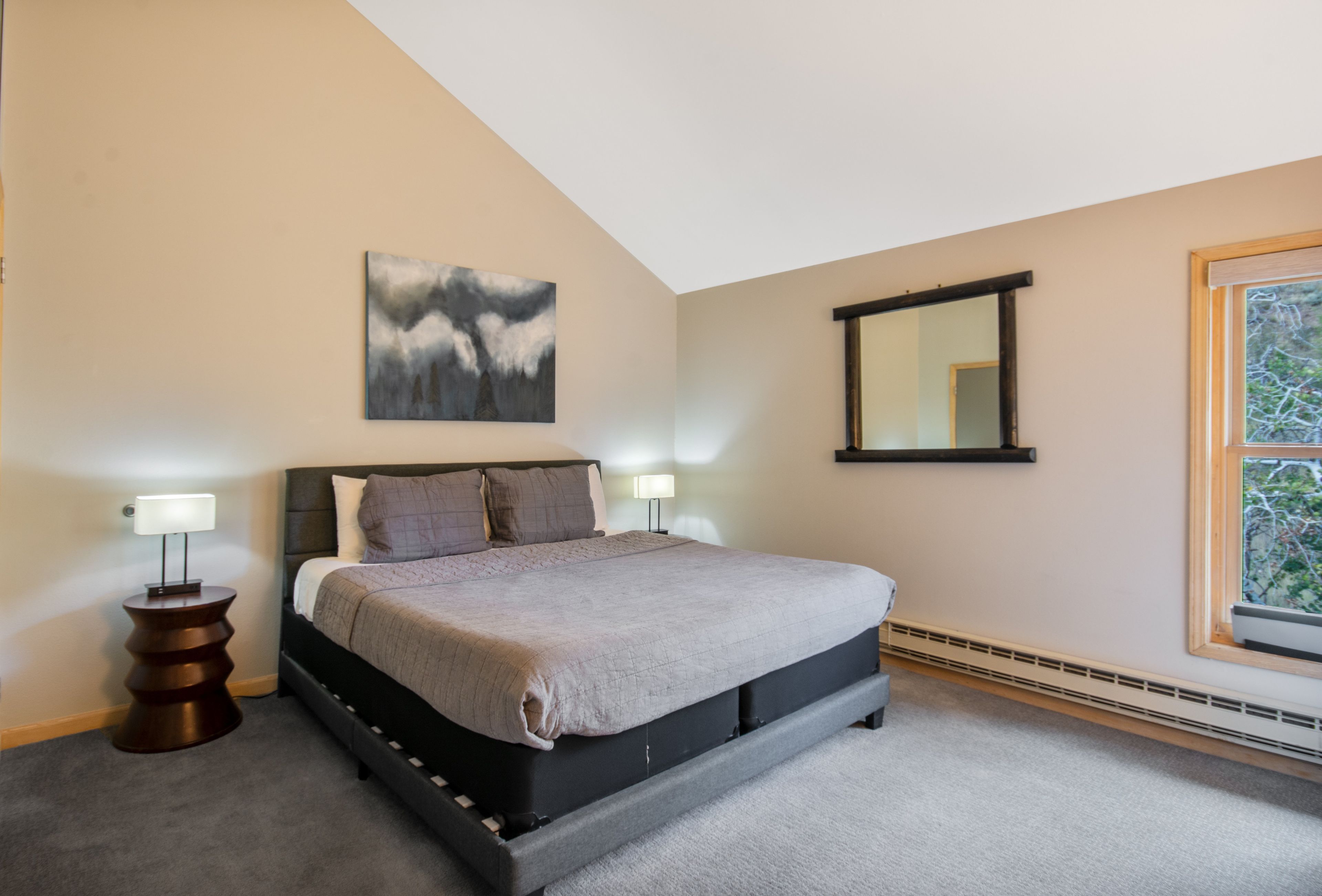 Een slaapkamer met een bed, twee bedlampen, een schilderij, een spiegel en een raam.