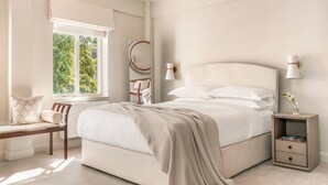 Un dormitorio con cama, mesitas de noche, una silla y una ventana con vista a la vegetación.