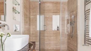 Un baño moderno con ducha envuelta en vidrio, un lavabo blanco y una encimera de mármol.