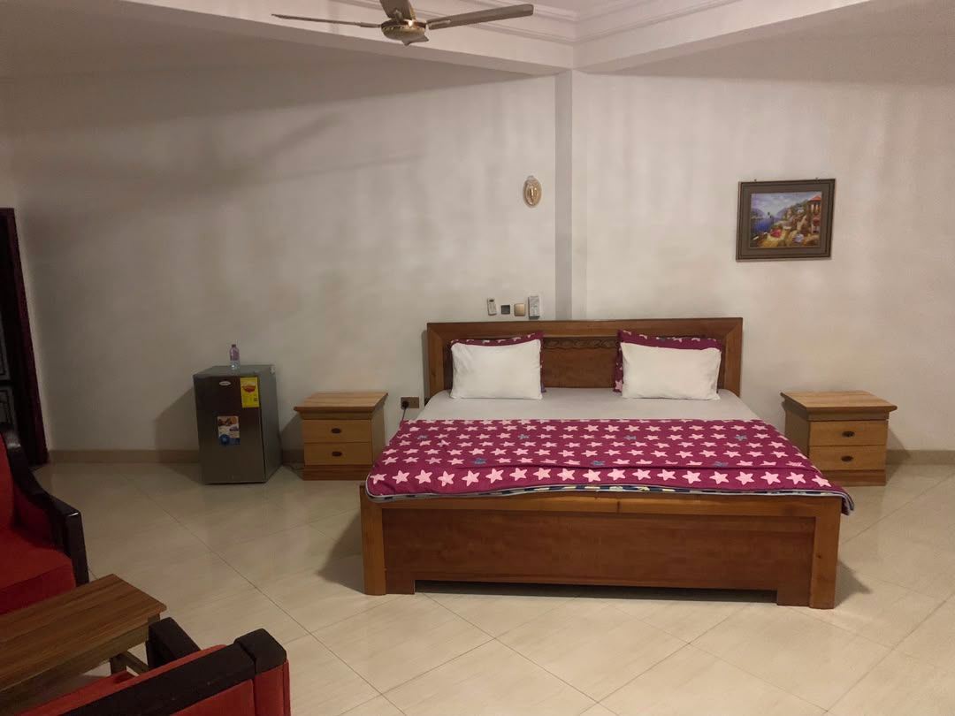 Ein Schlafzimmer mit einem hölzernen Bett, zwei Nachttischen, einem kleinen Safe und einem Deckenventilator.