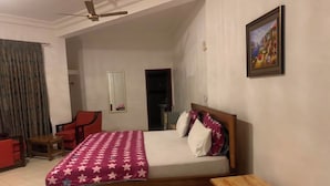 A bedroom with a bed, a wooden nightstand, a ceiling fan, a painting on the wall, and a door leading to another room. - MILANO INN HOTEL (AHODWO DABAN)