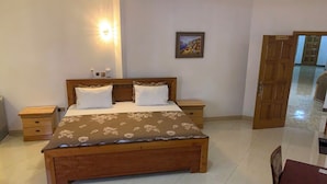 A bedroom with a wooden bed, bedside tables, a nightstand, a painting on the wall, and a door leading to another room. - MILANO INN HOTEL (AHODWO DABAN)