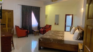 A hotel room with a bed, two chairs, a desk, and a window with curtains. - MILANO INN HOTEL (AHODWO DABAN)