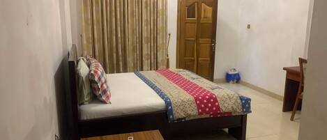 Ein Schlafzimmer mit einem Bett, einem Holztisch, einem Stuhl, einem Schrank und einer Tür.